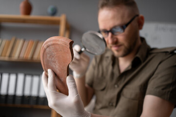 Portrait of a male archaeologist studying finds using a magnifying glass working in an office...
