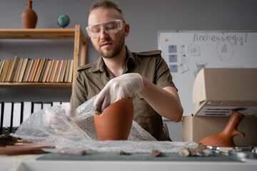 Archaeologist working with ancient finds working in the office packing an antique vessel to be sent...