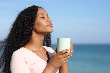 Black woman smelling coffee on the beach