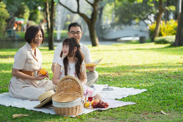 Happy family having picnic in the park with parents and kids sitting on the grass and enjoying healthy meals outdoors on a sunny summer day.