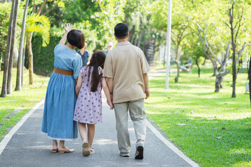 Fototapeta premium Happy Asian family holding hands and walking, enjoying leisure time with outdoor activities in a public park.