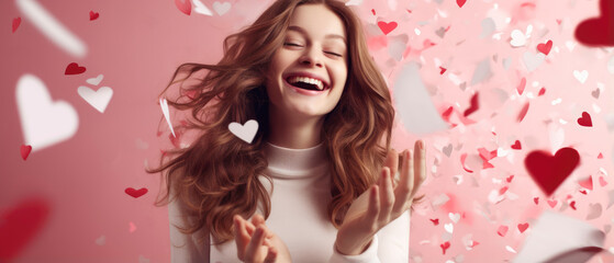 Excited positive girl smiling and looking at falling heart paper in Valentine day on pink background