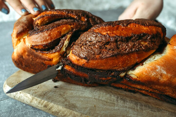 A woman cuts a homemade cinnamon roll with a knife on a kitchen cutting board.