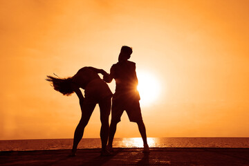 latin hispanic couple is dancing bachata above sea on summer beach. Sunset over water.Two silhouettes against the sun. Just married couple hugging. Romantic love story. Man and woman in holiday trip