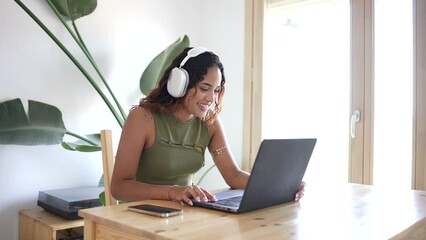 Happy woman working from home. In a wood-crafted haven, a girl immersed in work, laptop and headphones in a minimalist home with a touch of green. Focus and nature's serenity. Minimalist work space.