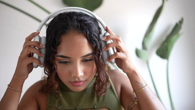 Woman putting on headphones. In a minimalist haven, a girl adorns sleek design headphones, merging style with simplicity. A harmonious blend in the modern sanctuary with a plant in the background.
