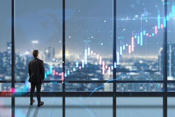Attractive young european businessman standing, and thinking on blurry night city background through window with forex chart. Double exposure.
