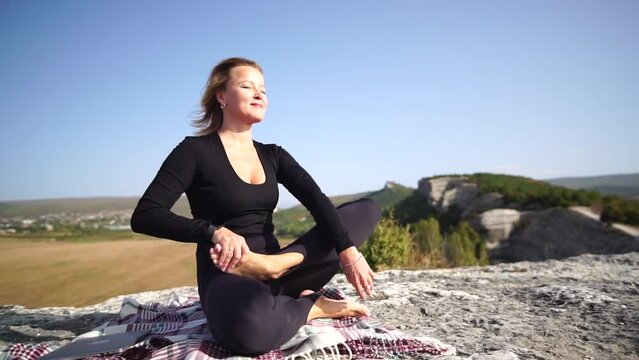 Woman yoga nature. Healthy happy middle aged woman in lotus pose or sukhasna meditating on mountain top. Serene yoga and pranayama practice, finding inner peace, relax body and mind in nature outdoors