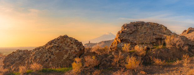 Wide angle view of sunrise with Ararat mountains and the Khor Virap monastery between two giant boulders at fall. Travel destination Armenia