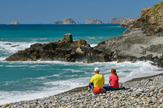 France, Brittany, Two hikers relaxing on rocky Porzh Mel beach