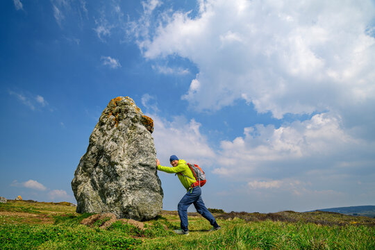 France, Brittany, Hiker pretending to push large menhir along Sentier Cotier route