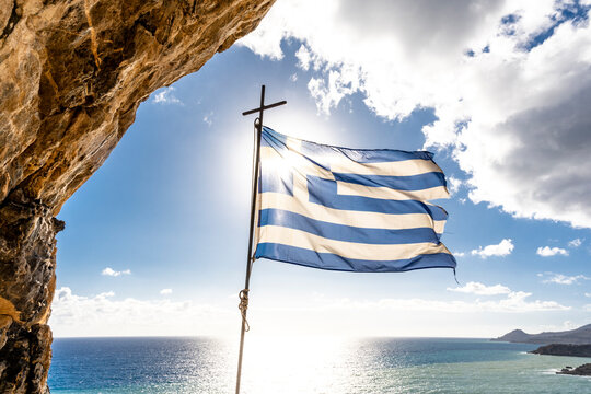 Greece, Crete,Greek flag fluttering against sun shining overMediterranean Sea