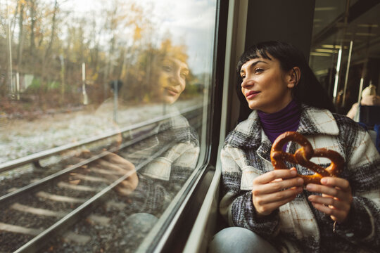 Contemplative woman holding pretzel and looking through window of train
