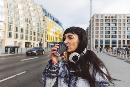 Woman drinking coffee standing on street in city