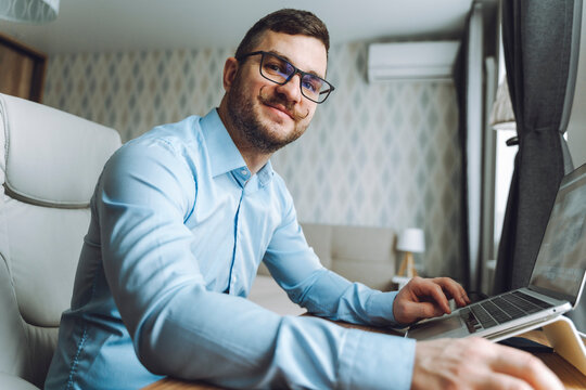 Smiling freelancer wearing eyeglasses and sitting with laptop at home office