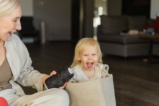 Cheerful girl in basket next to grandmother holding yarn spool at home