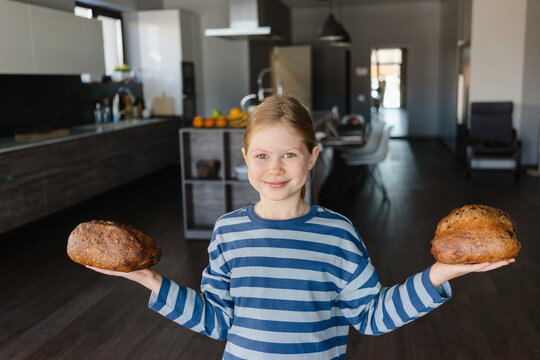 Smiling girl holding baked bread in hands at home