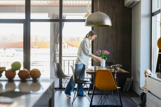 Woman arranging flower vase and setting dining table at home