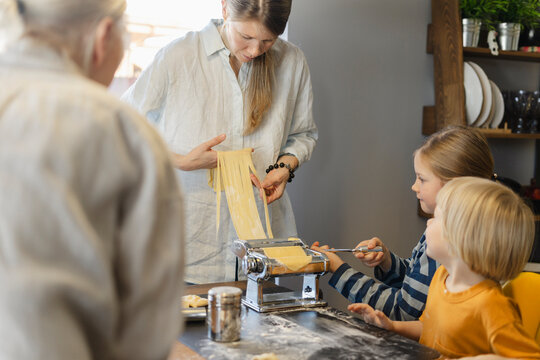 Woman cutting dough in pasta maker with family at home