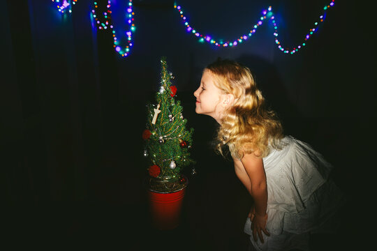 Smiling girl smelling decorated Christmas tree near string lights