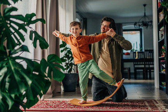 Smiling father helping son to balance on board at home