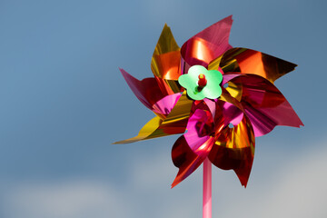 A colourful windmill for children spins in front of a blue sky with clouds. The sun is shining. The...