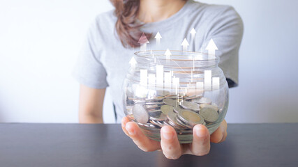 close up hand holding money into a glass jar for future savings and investment. Concepts about...