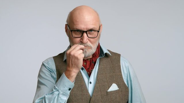 Middle-aged man in stylish attire making a zip your lip gesture, signifying secrecy. He has a composed expression with a light grey background. RED 8K RAW.