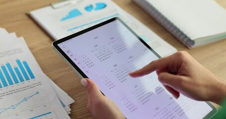 Manager leafing through yearly calendar in digital tablet at table with documents closeup 4k movie slow motion
