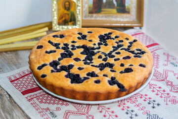 Lean yeast-free rice flour pie with blueberries on a towel with patterns on the background of icons and church candles, food for fasting before Easter