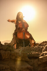 Woman playing cello in nature with sunset sunlight behind her