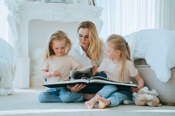 Attentive mother reading a book with her two young daughters on the floor, fostering a love for...