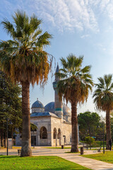 Fototapeta na wymiar Green mosque (yesil camii) and its turquoise color minaret. Square and park with palm-trees. Nicaea (iznik) in sunny day. Vertical shot. Bursa, Turkey