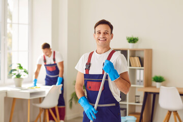Young male cleaner in overall, happy smiling man performing cleaning duties, professional team busy sanitizing, sweeping, polishing, mopping floor, house cleaning services for home, office