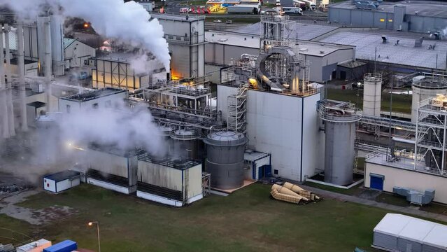 From above, a factory's smoking stacks stand out against additional yellow lighting, hinting at chemical production.