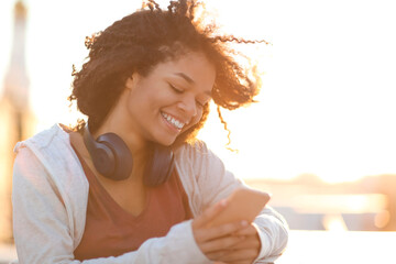 Outdoor portrait of happy cheerful african american woman in headphones using smartphone