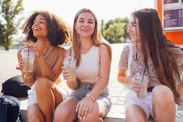 Cute teenage girls in casual summer clothes drinking tasty iced lemonade outdoors in the park.
