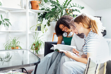 Three pretty female teenagers of different nationalities are reading a magazine and smiling