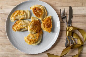 Roasted fryed Varenyky, vareniki, pierogi, pyrohy or dumplings, filled with cheese and potatoes, on grey gray plate on wooden background. Ukrainian traditional food