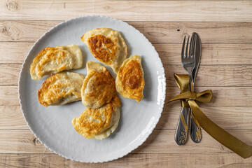 Roasted fryed Varenyky, vareniki, pierogi, pyrohy or dumplings, filled with cheese and potatoes, on grey gray plate on wooden background. Ukrainian traditional food