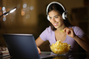 Happy woman in the night watching video eating potato chips