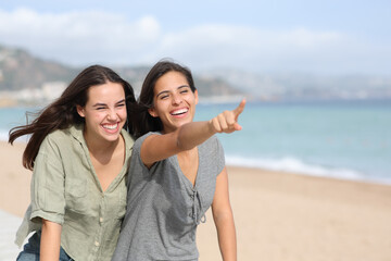 Two friends laughing and pointing away on the beach