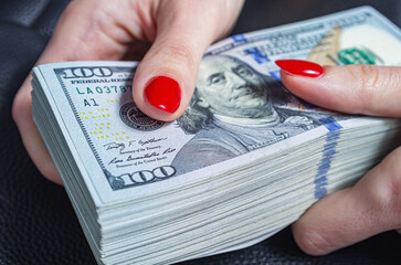 Woman's hands holding and counting US dollar bills. Stack of new hundred dollars banknotes.