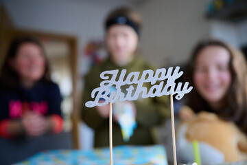 Drei unerkennbare Personen vor einem Geburtstagskuchen mit dem Schild 