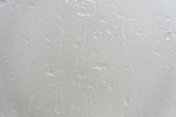 drops of rainwater running down the glass, sun showing on the outside.