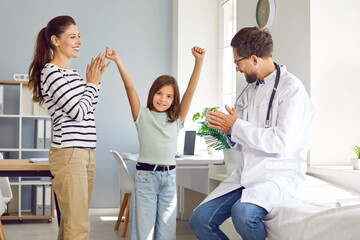 Male pediatrician and happy mother applaud little girl during appointment in medical office....