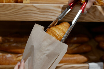 the seller puts the croissant in a paper bag