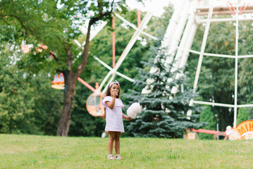 Child girl in an amusement park in the summer eats cotton candy and smiles happily. The concept of summer holidays and school holidays