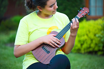 Cute teen girl playing her ukulele outdoors