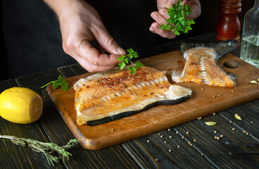 We prepare fresh red fish in the restaurant kitchen before salting with aromatic spices. Chef hand adding parsley to fish steak